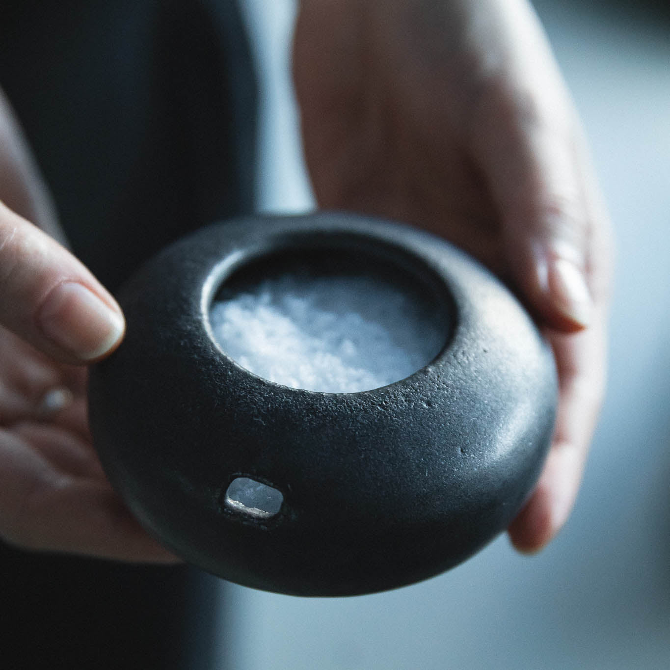 Hand holding a dark ceramic bowl with a blurred background
