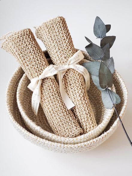 Knitted items in a woven basket with a sprig of eucalyptus on a light background