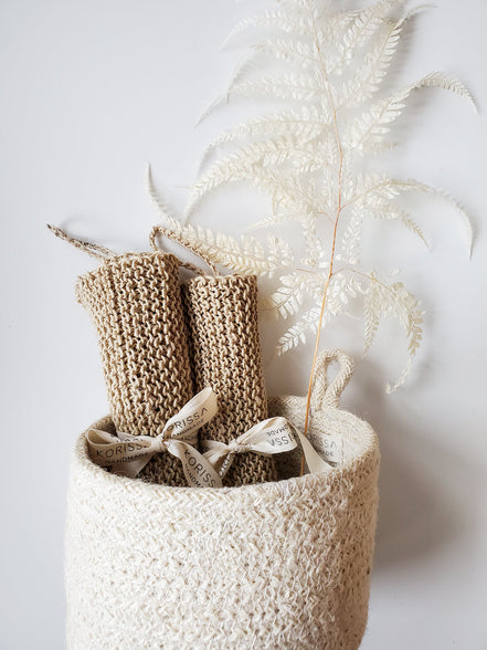 Knitted hemp wasclothes in a textured basket with dried plants on a light background