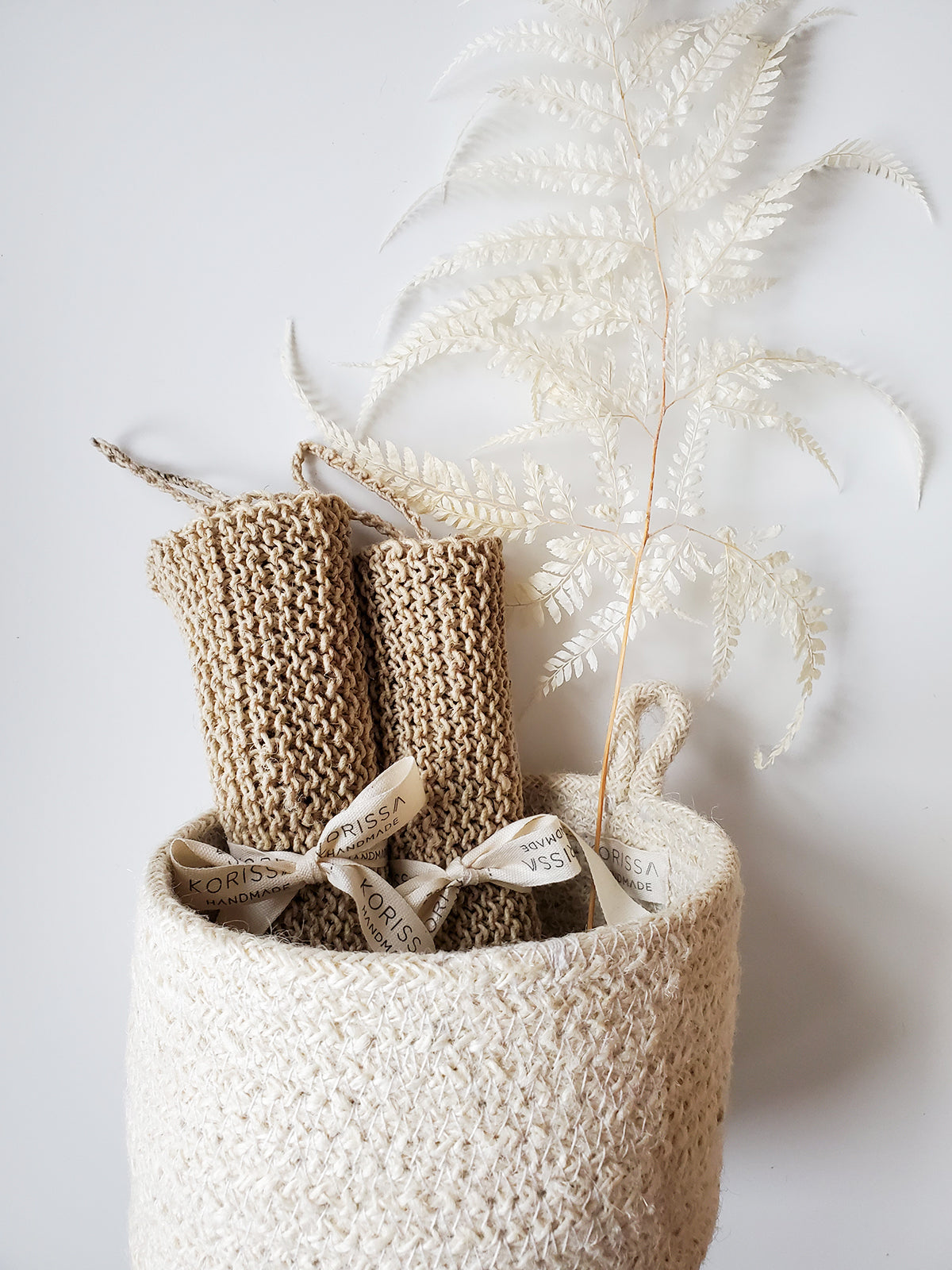 Knitted hemp wasclothes in a textured basket with dried plants on a light background
