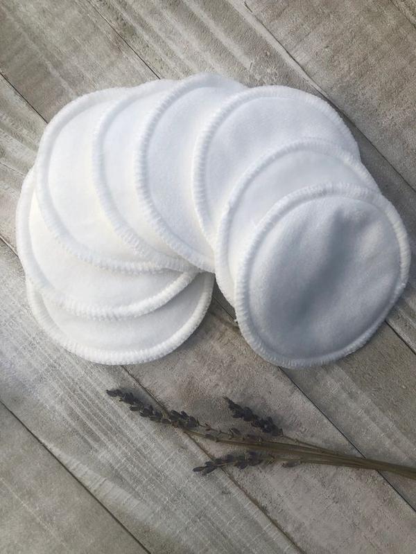 Stack of white reusable menstrual pads on a wooden surface with lavender flowers.