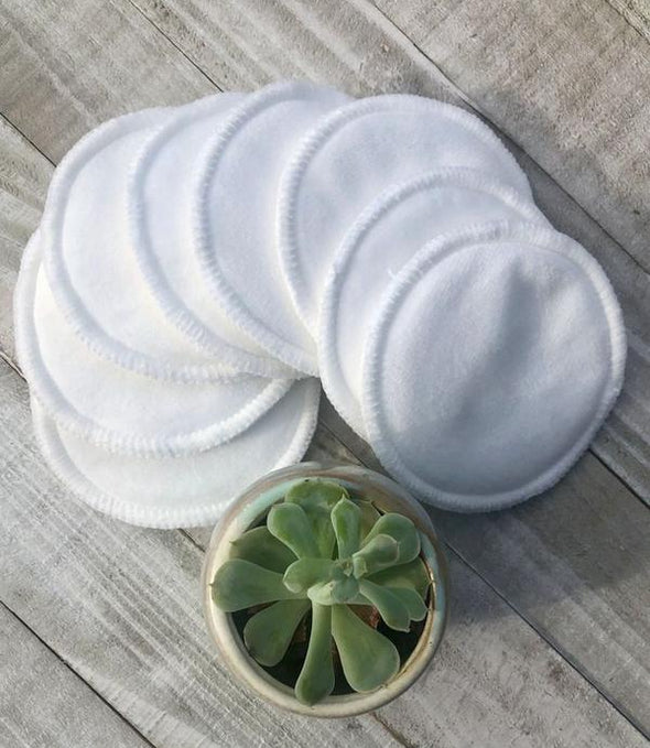 Stack of white reusable makeup pads on a wooden surface with a small potted plant.